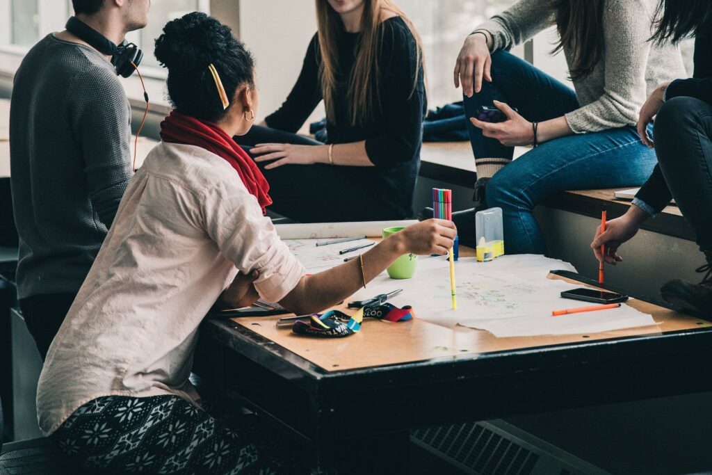 5 étudiants à l'université qui font leur rentrée à l'université autour d'une table ils travaillent en groupe de façon détendue et décontractée sans stress avec des feuilles et des surligneurs sur la table