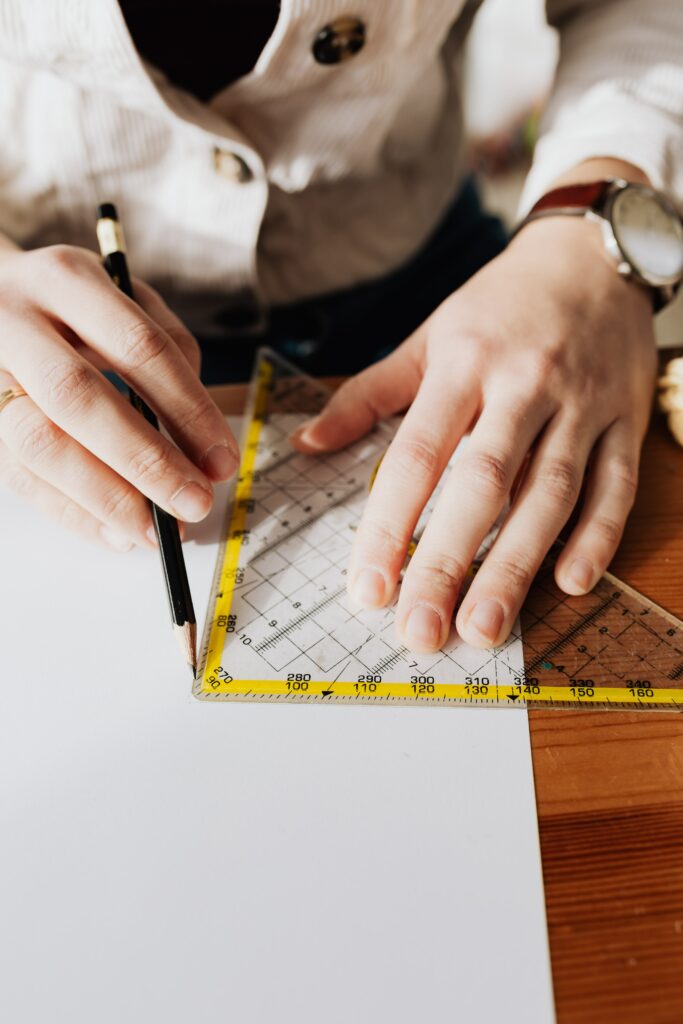 personne sur une table qui mesure les dimensions de son mémoire pour l'imprimer sur mesure les mains tracent un trait avec une équerre au crayon à papier