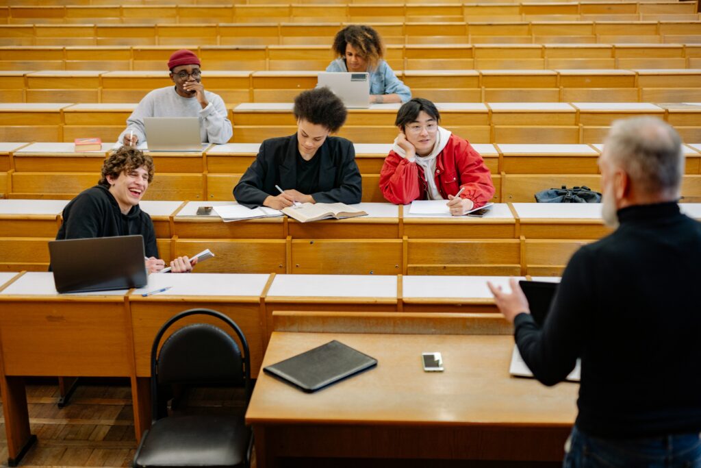 directeur de mémoire de dos qui donne cours à 5 étudiants dans un amphi avec des bancs marrons 