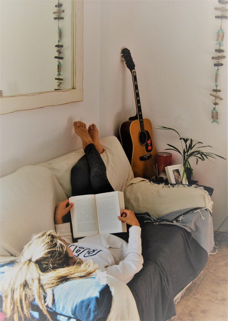 étudiante qui lit un livre dans un canapé beige avec une guitare au bout posée contre le mur 