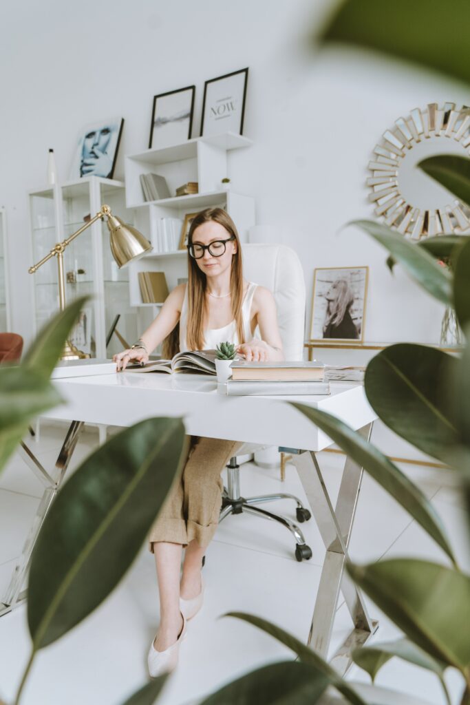 étudiante plantes bureau blanc cadre derrière elle qui lit un magazine